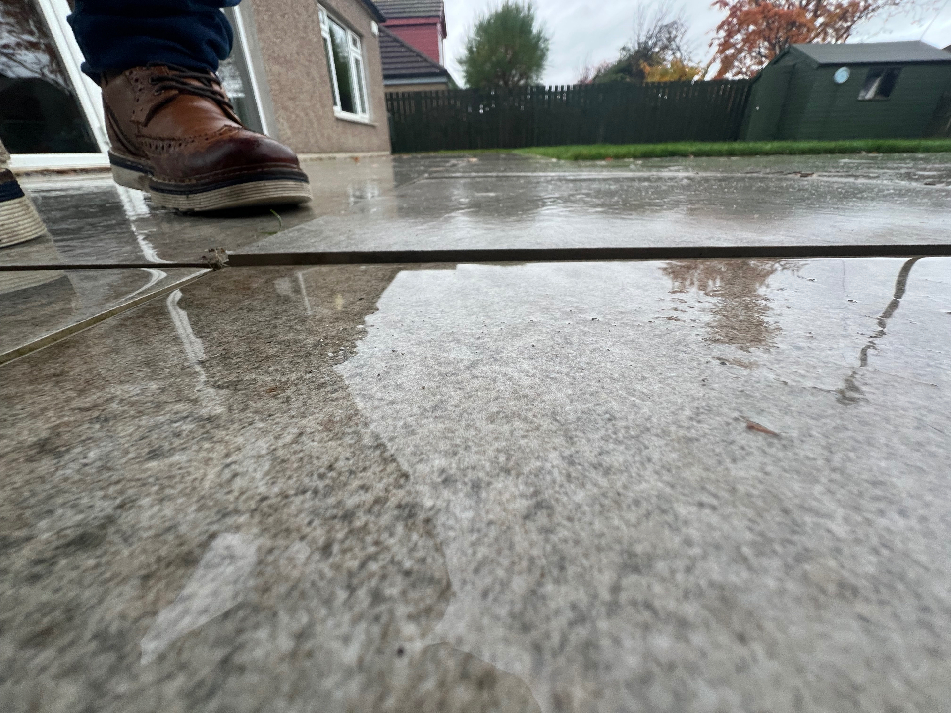 Water pooling on poorly installed porcelain paving showing inadequate drainage fall and surface flooding typical of substandard installations in Edinburgh