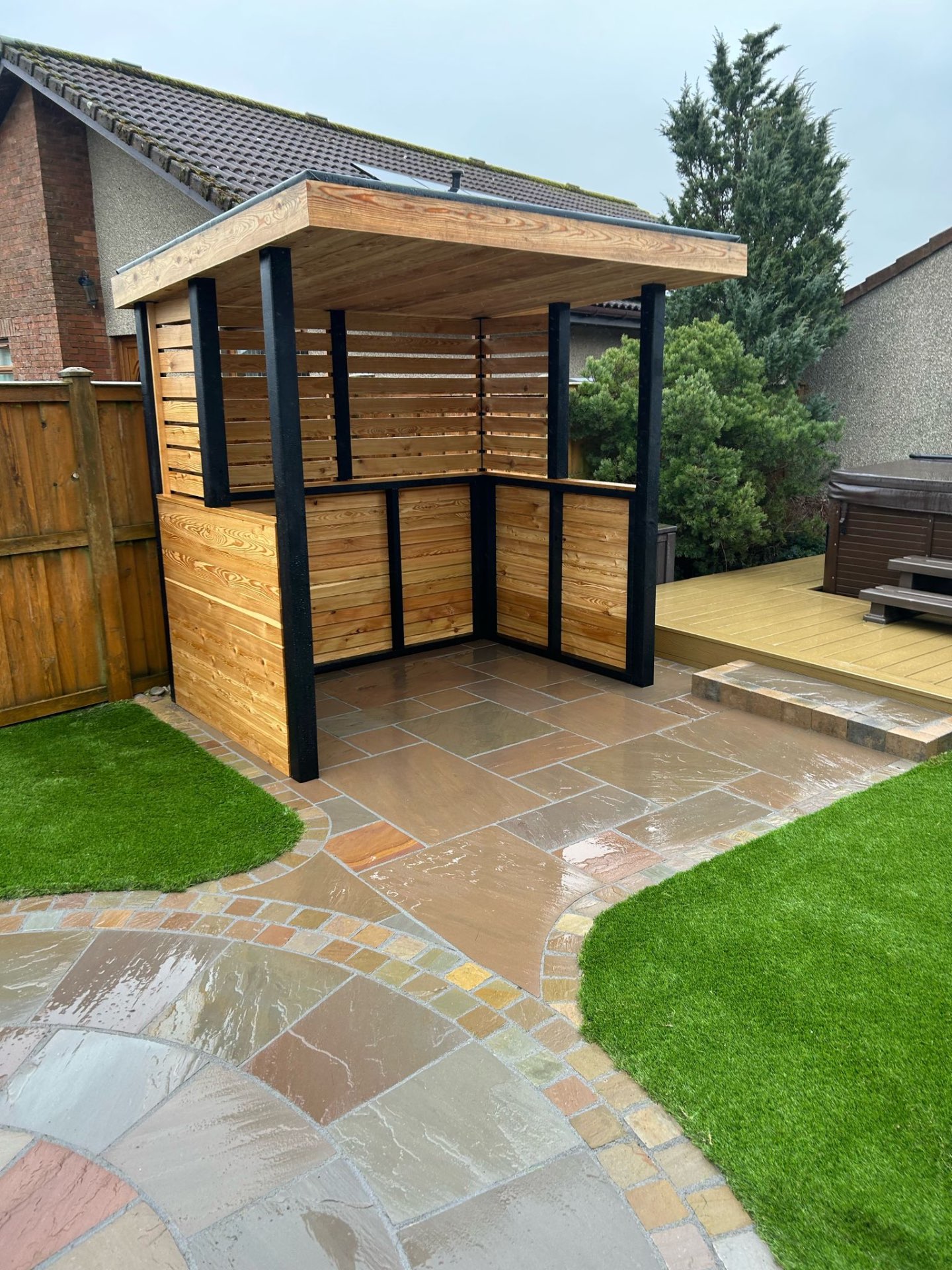 Indian sandstone patio with timber pergola and artificial grass in Scottish garden by Maybury Landscaping