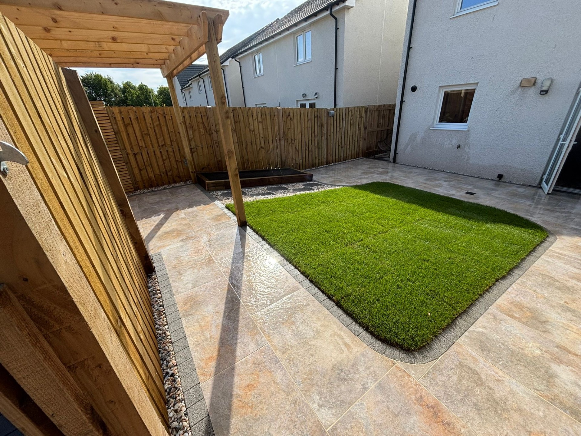 Timber pergola and Venetian-style slatted fencing above a turf lawn and Burlington Ivory porcelain patio in West Craigs, Maybury, Edinburgh