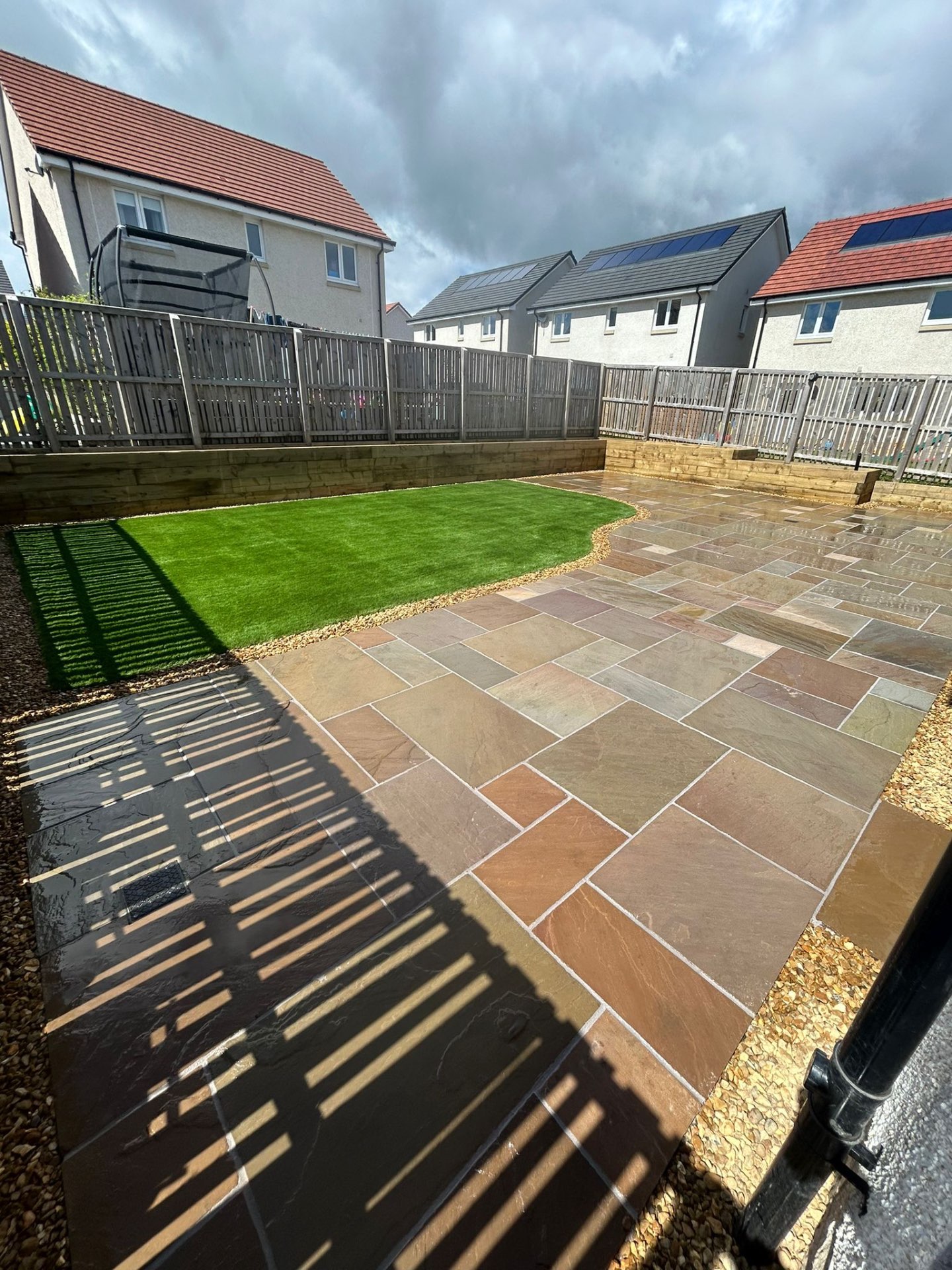 Wide view of completed Winchburgh garden showing sandstone patio, artificial grass, and timber raised beds