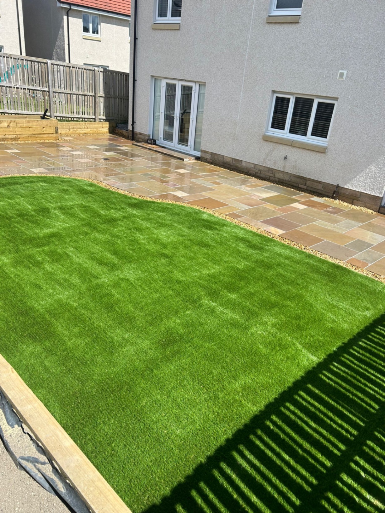 Premium artificial grass installation adjacent to multi-tone sandstone patio in Winchburgh