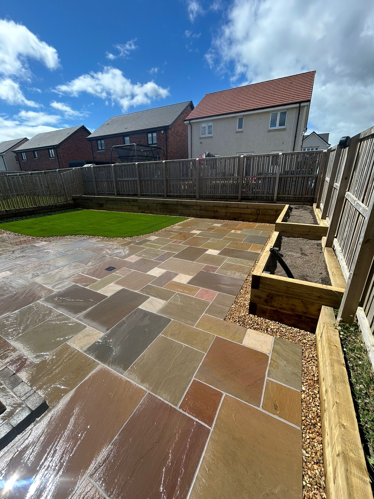 Professional raj green multicolor Indian sandstone patio installation in Scottish residential garden with vibrant natural color variations and timber sleeper edging