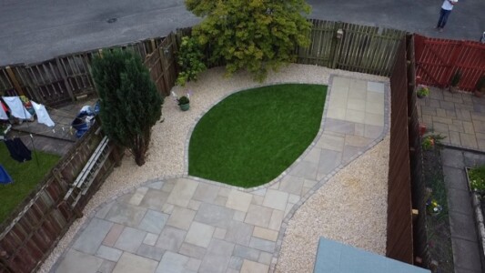 Alt text: A beautifully designed patio installation in Alloa featuring Indian sandstone paving and artificial grass, surrounded by decorative stones. Garden Landscaping Edinburgh, Garden Landscaping Alloa, Patios and Paving Alloa, Patios and Paving Edinburgh
