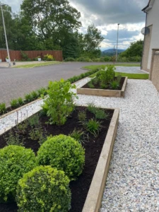 "An image showing the installation process of a raised sleeper bed in a garden. The workers are carefully positioning and securing the wooden sleepers to create the structure of the bed. The bed is being filled with rich, fertile soil, ready for planting. The raised bed will provide a designated area for gardening, offering easy access and improved drainage for plants. The installation is being carried out with precision and expertise, ensuring a sturdy and attractive addition to the garden landscape."