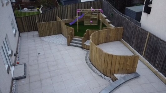 A beautifully designed patio made from porcelain tiles, accompanied by vertical timber sleepers to create a stylish and modern outdoor space in Alloa." "A vibrant and lush artificial grass installation, perfect for a children's play park in Alloa. The artificial grass provides a safe and low-maintenance surface for kids to play on, creating a vibrant and enjoyable outdoor environment."