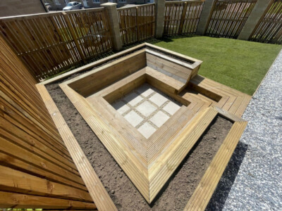 "Inviting sunken seating area in Dunfermline featuring sleeper frame, timber deck board seating, and cream porcelain tiles in the center. Completed with topsoil and turf for a lush and comfortable outdoor space."